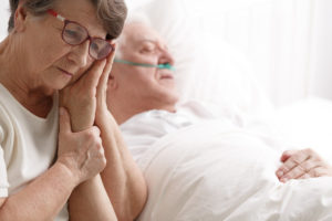 Sad senior woman holding her dying husband's hand