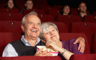 Senior Couple Watching Film In Cinema Laughing And Eating Popcorn